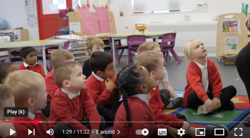 reception aged children in red jumpers participating in a phonics demo lesson